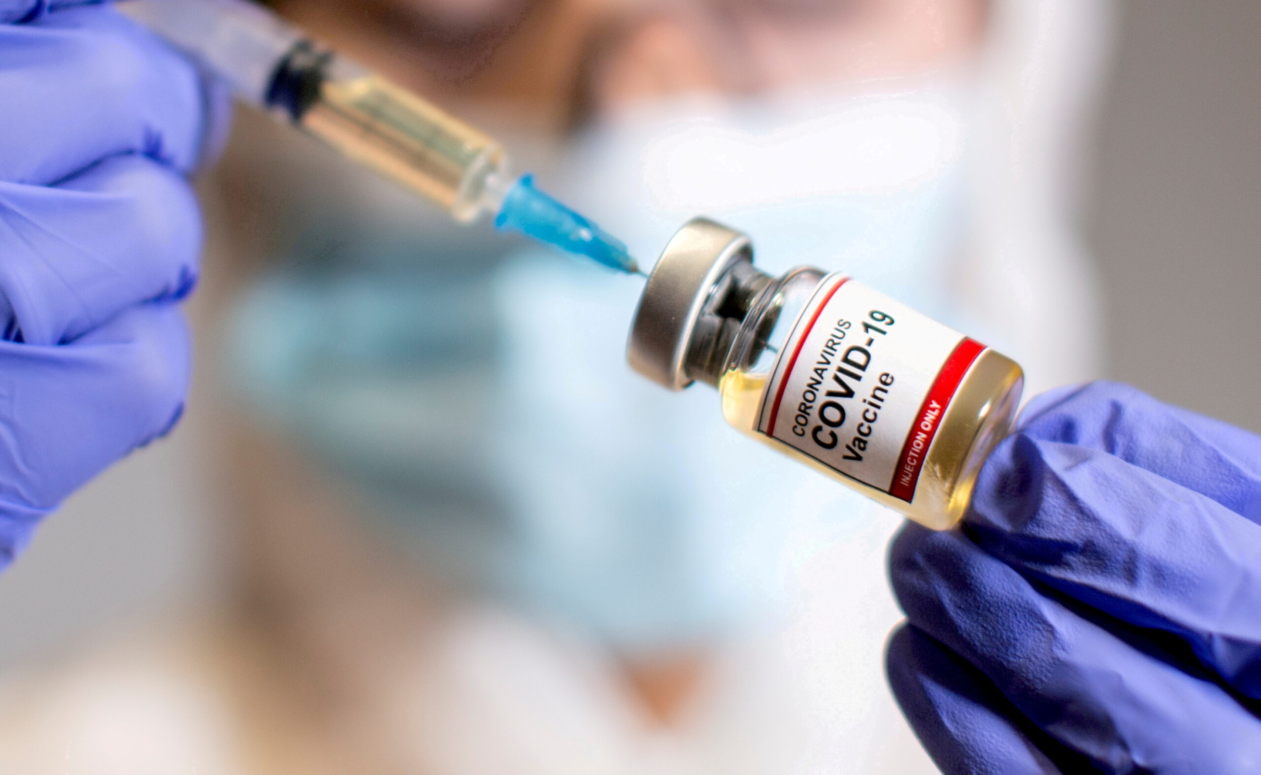 m_FILE PHOTO: A woman holds a medical syringe and a small bottle labelled "Coronavirus COVID-19 Vaccine