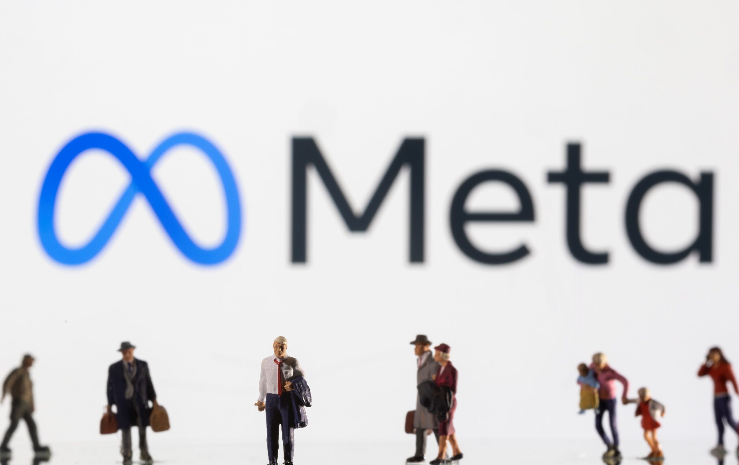 Illustration shows small figurines and displayed Meta logo